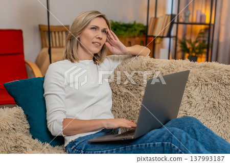Woman massaging temples on sofa at home, feeling tired from long work on laptop headache discomfort Woman massaging temples on sofa at home, feeling tired from long work on laptop headache discomfort 137993187