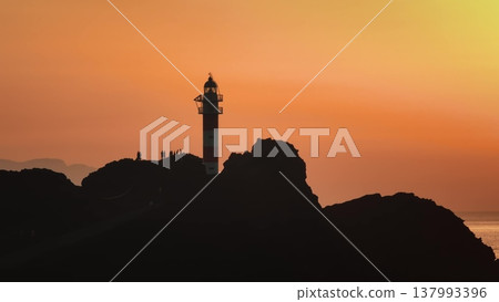 Tourists silhouette against vibrant sunset at Punta de Teno lighthouse, showcasing a stunning coastal view under bright orange sky. Tenerife, Canary Islands. Drone flight panorama Tourists silhouette against vibrant sunset at Punta de Teno lighthouse, showcasing a stunning coastal view under bright orange sky. Tenerife, Canary Islands. Drone flight panorama 137993396