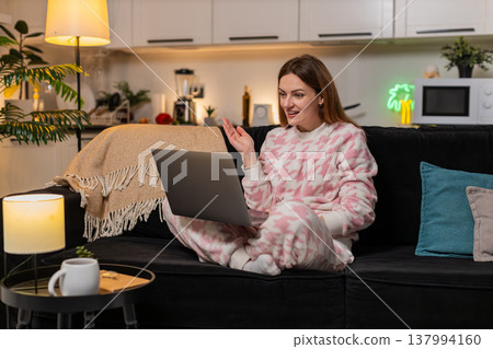 Adult woman on laptop video call waves hello smiles shares news live chat at night Adult woman on laptop video call waves hello smiles shares news live chat at night 137994160