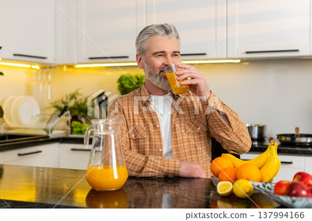 Middle-aged man pouring fresh orange juice and enjoying healthy diet lifestyle drink in home kitchen Middle-aged man pouring fresh orange juice and enjoying healthy diet lifestyle drink in home kitchen 137994166