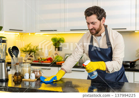 Middle-aged man smiling while cleaning kitchen table with cloth for home hygiene and freshness daily 137994225