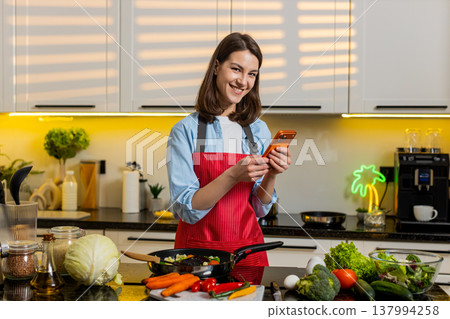 Young woman smiling at smartphone in kitchen planning healthy diet meal prep for weight loss at home Young woman smiling at smartphone in kitchen planning healthy diet meal prep for weight loss at home 137994258