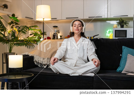 Young woman in headphones meditates to rain sounds deep breathing calm mind quiet mood evening sleep 137994291