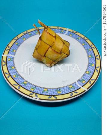 Golden rice cake rests on a patterned plate. Bright blue background contrasts vividly with the food. Clean, minimalist setup draws attention to the dish. Ideal for culinary, cultural 137994503