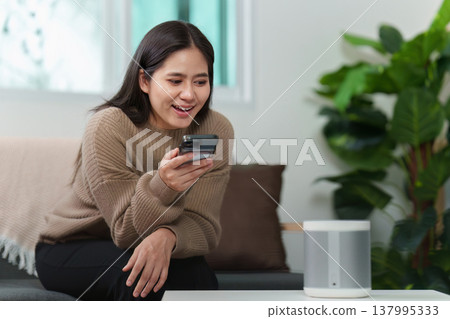 Woman using smartphone to interact with smart speaker Woman using smartphone to interact with smart speaker 137995333