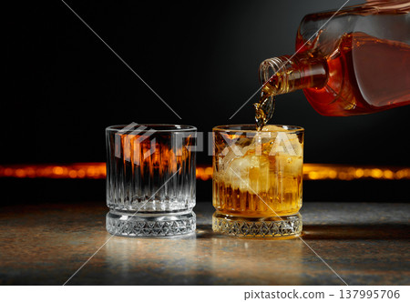 Whiskey is poured into a glass with ice. Whiskey is poured into a glass with ice. 137995706