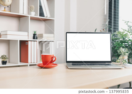 Modern office desk with blank laptop screen mockup, red coffee cup and plant near bookshelf, clean workspace background with copy space for branding, technology, productivity, remote work. mockup Modern office desk with blank laptop screen mockup, red coffee cup and plant near bookshelf, clean workspace background with copy space for branding, technology, productivity, remote work. mockup 137995835