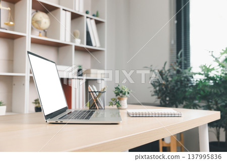Modern coworking desk with blank laptop screen mockup, notebook and pen cup, small plant and bookshelf background. Clean office workspace with copy space for branding, productivity. mockup, blank Modern coworking desk with blank laptop screen mockup, notebook and pen cup, small plant and bookshelf background. Clean office workspace with copy space for branding, productivity. mockup, blank 137995836