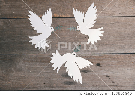 Three white paper-cut doves with olive branches on rustic wooden planks, flat lay with copy space. Minimal peace and unity symbol for charity campaigns, posters, greetings worldwide. peace, unity Three white paper-cut doves with olive branches on rustic wooden planks, flat lay with copy space. Minimal peace and unity symbol for charity campaigns, posters, greetings worldwide. peace, unity 137995840