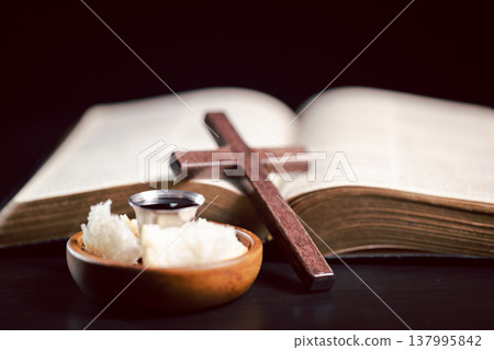 Still life of communion bread and silver cup of red wine with wooden cross on dark table, symbolizing Christian Eucharist, worship, faith, sacrifice and remembrance with copy space. 137995842