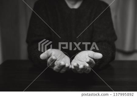 Black and white close-up of clasped hands resting on a table, suggesting prayer, contemplation and quiet faith. Minimal background with copy space for message. Spiritual mood for inspirational text. Black and white close-up of clasped hands resting on a table, suggesting prayer, contemplation and quiet faith. Minimal background with copy space for message. Spiritual mood for inspirational text. 137995892