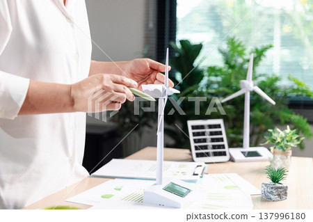 Business professional pointing at wind turbine model beside solar panel and ESG charts on desk, sustainable renewable energy strategy, green finance planning, eco corporate reporting, copy space. Business professional pointing at wind turbine model beside solar panel and ESG charts on desk, sustainable renewable energy strategy, green finance planning, eco corporate reporting, copy space. 137996180