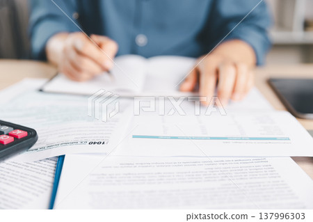 Close-up tax forms on office desk accountant signs paperwork with pen and calculator, reviewing income return filing, accounting compliance, audit preparation, budgeting, deadline.tax, income, return Close-up tax forms on office desk accountant signs paperwork with pen and calculator, reviewing income return filing, accounting compliance, audit preparation, budgeting, deadline.tax, income, return 137996303
