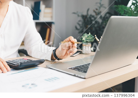 Business analyst reviewing financial report on laptop with calculator and chart documents at office desk, budgeting and accounting for corporate finance, audit, tax and investment planning. financial Business analyst reviewing financial report on laptop with calculator and chart documents at office desk, budgeting and accounting for corporate finance, audit, tax and investment planning. financial 137996304