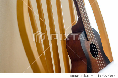A close-up of a ukulele placed on a wooden chair. 137997562
