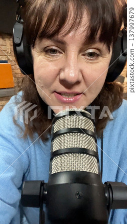 woman with headphones sits in front of a microphone and speaks woman with headphones sits in front of a microphone and speaks 137997679