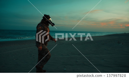 Soldier walks on beach contaminated by radiation from nuclear attack at sunset 137997828