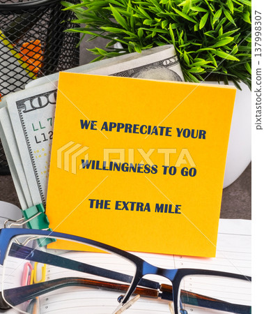 A vibrant yellow note expressing gratitude for exceptional effort rests amidst crisp 100 dollar bills, green plant, and eyeglasses on a clean office desk A vibrant yellow note expressing gratitude for exceptional effort rests amidst crisp 100 dollar bills, green plant, and eyeglasses on a clean office desk 137998307