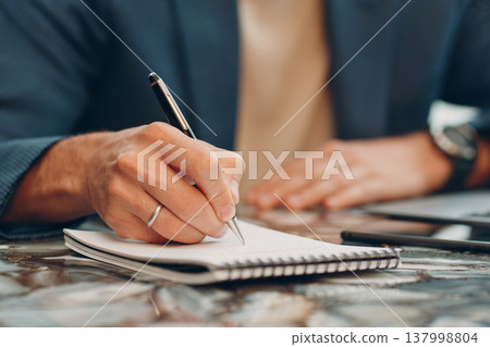 A businessman writes a business plan in a notebook. A man writes an idea with ballpoint pen. 137998804