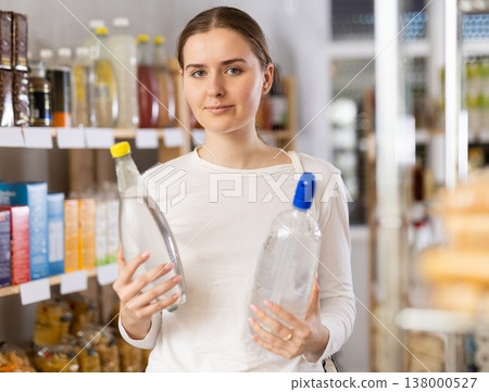 Girl customer in supermarket examines soda bottle, chooses food-stuff in grocery Girl customer in supermarket examines soda bottle, chooses food-stuff in grocery 138000527
