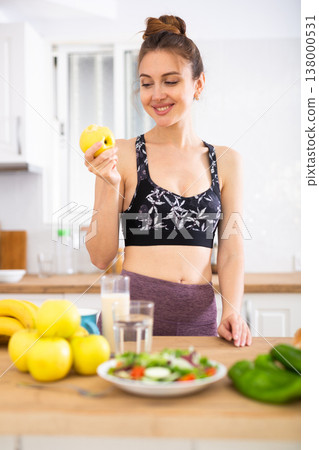 Young sportive woman eating apple in kitchen 138000531