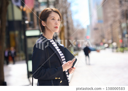 一位三十多歲的日本女商人，身穿海軍藍西裝外套，走在街上。 138000583