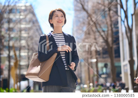 一位三十多歲的日本女商人，身穿海軍藍西裝外套，走在街上。 138000585