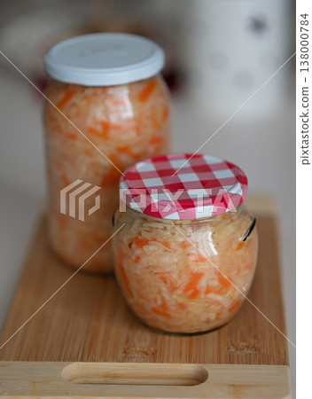 Jars of fermented sauerkraut with carrots on wooden cutting board in kitchen setting 138000784