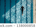 Diver in sleek black suit gracefully plunges into clear blue water creating ripples and splashes 138000858