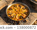 Vibrant seafood paella cooking in a traditional pan over an open flame with rich colors and textures 138000872