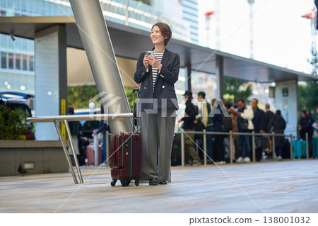 一位三十多歲的日本女商人拖著行李箱在城裡四處走動。 一位三十多歲的日本女商人拖著行李箱在城裡四處走動。 138001032