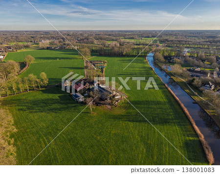 Aerial view of a traditional Dutch farmstead nestled among vibrant green fields and a calm canal in Dinxperlo, Netherlands. Beautiful rural landscape under a clear sky at golden hour. Aerial view of a traditional Dutch farmstead nestled among vibrant green fields and a calm canal in Dinxperlo, Netherlands. Beautiful rural landscape under a clear sky at golden hour. 138001083