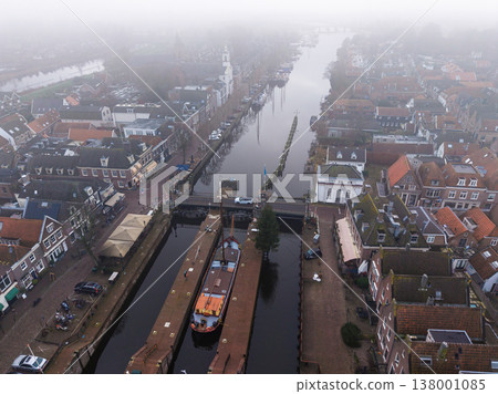Aerial view of a canal lock with a large boat, traditional brick houses, cobblestone streets and a festive Christmas tree, creating a charming small town winter atmosphere along the waterfront. Aerial view of a canal lock with a large boat, traditional brick houses, cobblestone streets and a festive Christmas tree, creating a charming small town winter atmosphere along the waterfront. 138001085