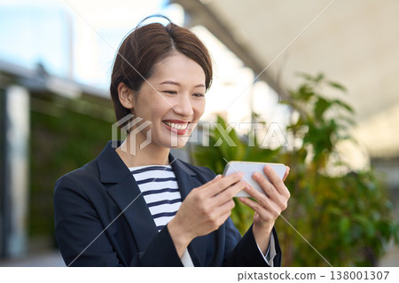 A Japanese businesswoman in her 30s looks happy while looking at her smartphone. A Japanese businesswoman in her 30s looks happy while looking at her smartphone. 138001307