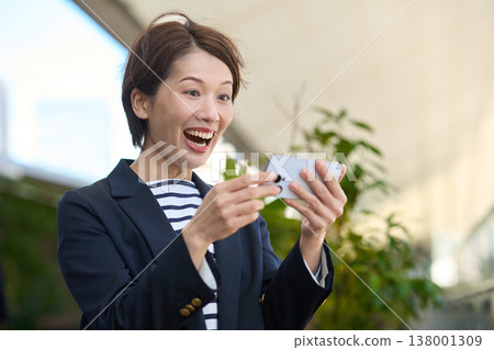 A Japanese businesswoman in her 30s looks happy while looking at her smartphone. A Japanese businesswoman in her 30s looks happy while looking at her smartphone. 138001309