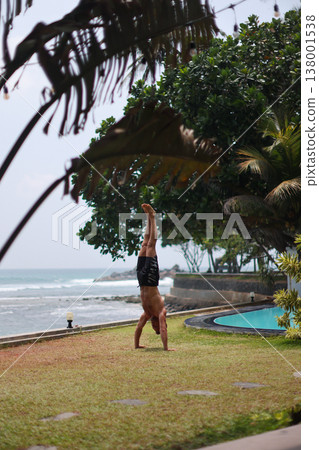 Man holding handstand on grass near ocean in tropical setting Man holding handstand on grass near ocean in tropical setting 138001538