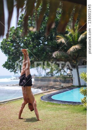 Man holding handstand on grass near ocean in tropical setting Man holding handstand on grass near ocean in tropical setting 138001545