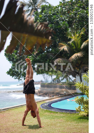 Man holding handstand on grass near ocean in tropical setting Man holding handstand on grass near ocean in tropical setting 138001546