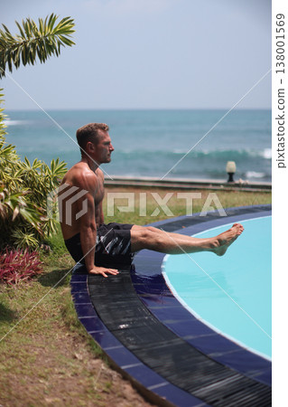 Athletic man performing L-sit exercise near pool with ocean view Athletic man performing L-sit exercise near pool with ocean view 138001569