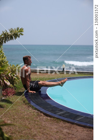 Athletic man performing L-sit exercise near pool with ocean view 138001572