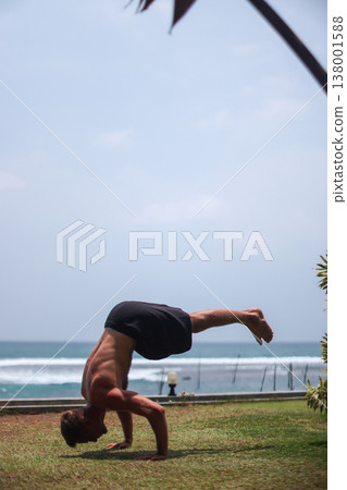 Athletic man practicing handstand near ocean and pool in tropical location 138001588