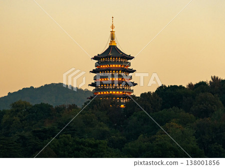 Traditional East Asian pagoda shining with warm lights at sunset, nestled among lush green trees on a tranquil hillside Traditional East Asian pagoda shining with warm lights at sunset, nestled among lush green trees on a tranquil hillside 138001856