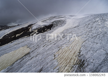 Aerial above cracked epic glacier Elbrus Caucasus mountain. Snow-capped highest peaks in fog clouds, glacier melting. Aerial above cracked epic glacier Elbrus Caucasus mountain. Snow-capped highest peaks in fog clouds, glacier melting. 138002243