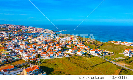 Drone view of a beautiful European city with a hilly landscape on ocean background. Aerial view of a small European town against blue sky and Atlantic Ocean.  Beautiful natural landscape. Portugal. 138003353
