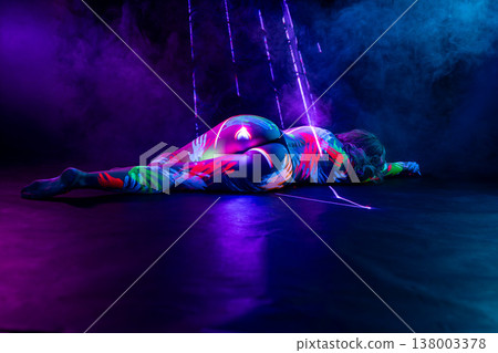 Woman with vibrant fluorescent body paint lying in dark studio with neon lights and smoke. Woman with vibrant fluorescent body paint lying in dark studio with neon lights and smoke. 138003378