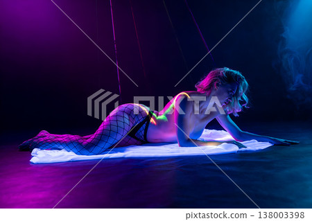 Sensual woman in fishnet stockings lying in a futuristic club setting with neon blue and pink lights, smoke, and red laser beams. Sensual woman in fishnet stockings lying in a futuristic club setting with neon blue and pink lights, smoke, and red laser beams. 138003398