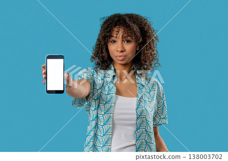 Smiling african teen woman showing smartphone white screen on blue. Mock-up 138003702