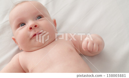 A sweet newborn boy lies on the sofa. Beautiful infant boy with blue eyes. Cute two-month-old baby resting in bed. High angle view of a chubby male kid. Closeup portrait of a calm baby. 138003881