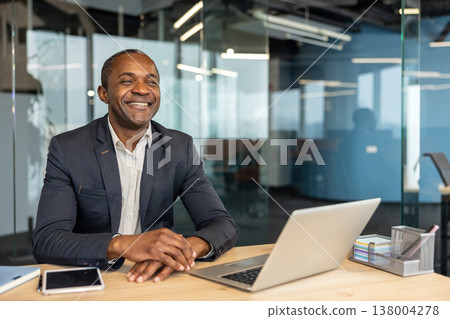 Happy adult man having a positive attitude while working with a laptop at his office, representing success, achievement, and a thriving business environment Happy adult man having a positive attitude while working with a laptop at his office, representing success, achievement, and a thriving business environment 138004278