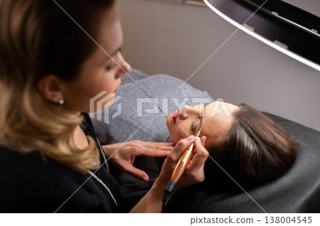 Young woman making tatouage for eyebrows in a dressing makeup room. Eyebrows make up process. Make-up artist in beauty studio doing makeup for beautiful girl. Making mua. Young woman making tatouage for eyebrows in a dressing makeup room. Eyebrows make up process. Make-up artist in beauty studio doing makeup for beautiful girl. Making mua. 138004545
